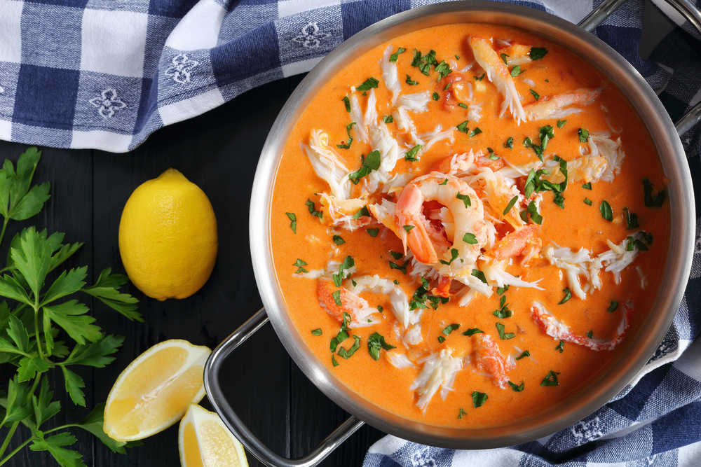 delicious hot bisque or thick soup of shredded snow crab meat, prawn, lobster in a stainless metal casserole on black wooden table with kitchen towel, authentic french recipe, view from above, close-up